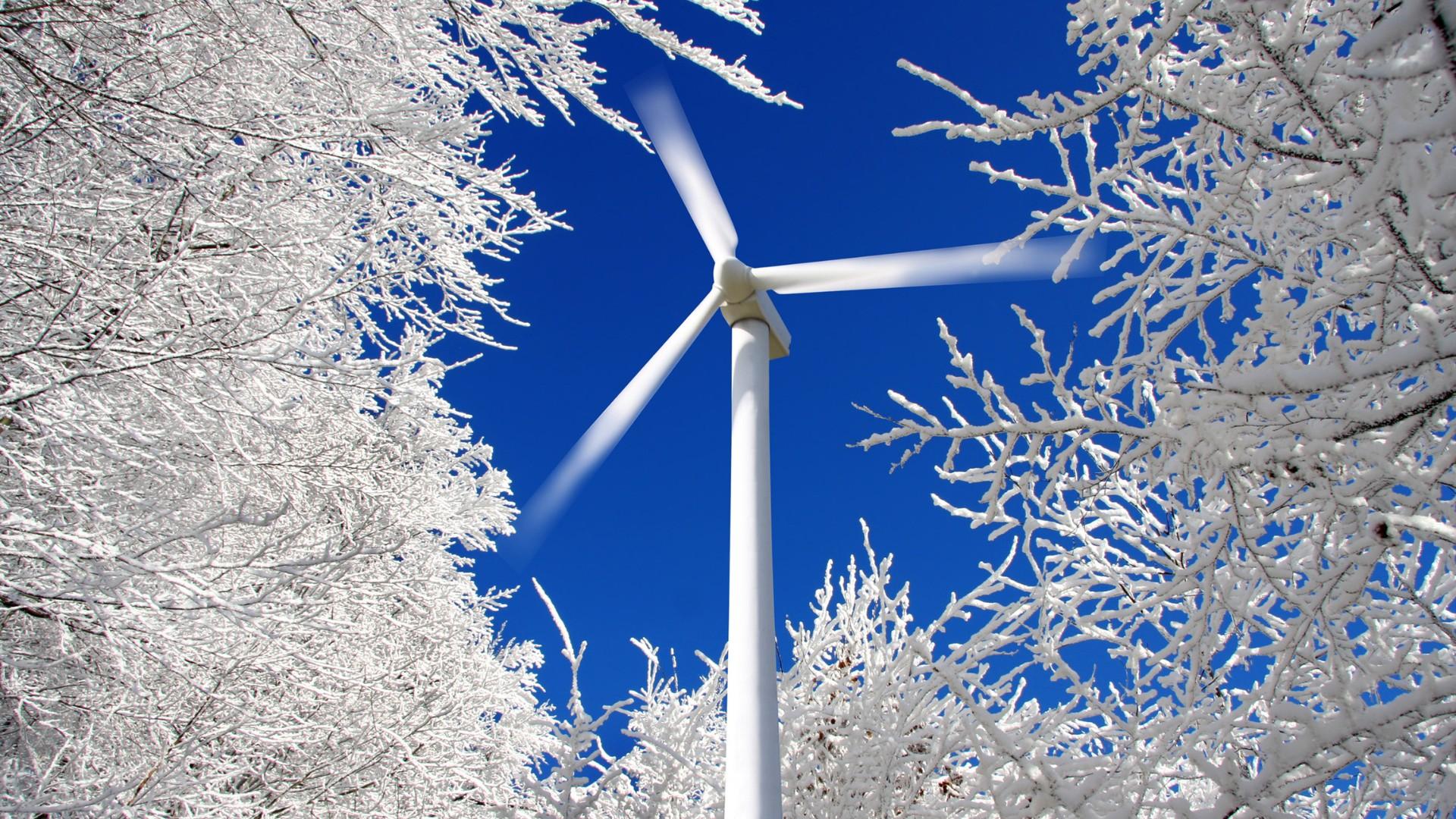 White wind turbine with snow-covered trees around the turbine.